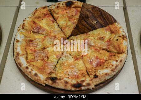 Pizza au jambon et fromage fraîchement cuit avec une fine croûte croustillante sur planche de bois. Pizza artisanale tranchée dans un authentique marché nocturne thaïlandais de Street food. Banque D'Images