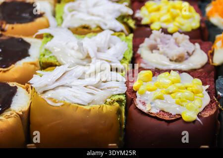 Petits pains fusion thaïlandais stylisés comme des sushis avec des garnitures de noix de coco, de maïs et de taro. Dessert de boulangerie coloré inspiré par la culture moderne de la Street food. Banque D'Images