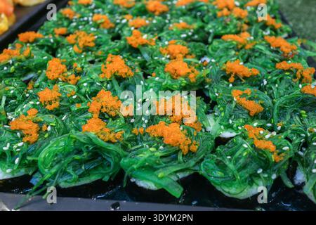 Sushis de cuisine de rue fusion japonaise avec salade d'algues vertes et œufs d'orange. Snacks asiatiques vibrants pour des applications alimentaires modernes et une marque culinaire tendance. Banque D'Images