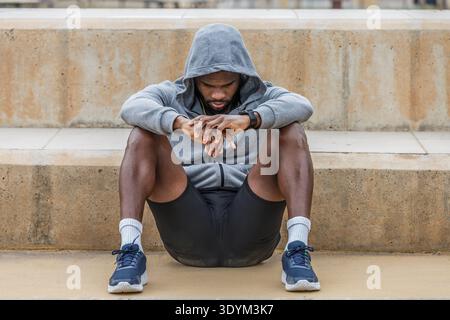 Corps complet de jeune athlète masculin afro-américain bouleversé assis la tête en bas sur le concept de défaillance au sol et de dépression Banque D'Images