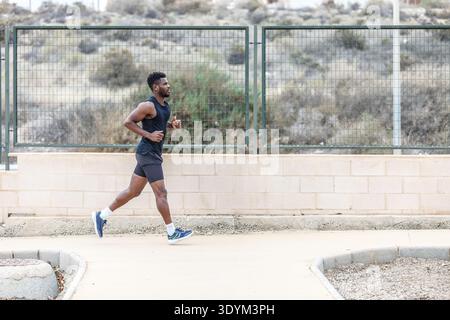 Vue latérale d'un sportif barbu ethnique en vêtements de sport et de baskets qui court pendant l'entraînement physique tout en regardant vers l'avant Banque D'Images