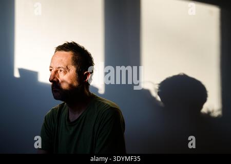 Portrait d'un homme barbu d'âge moyen avec un regard dramatique et intense, des ombres profondes façonnant son visage contre un intérieur sombre et flou. Mise au point sélective. Banque D'Images