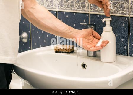 Appuyez à la main sur le flacon de pompe pour distribuer le savon mousse pendant que l'eau coule du robinet dans l'évier Banque D'Images