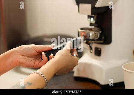 Gros plan des mains d'une barista détachant le porte-filtre rempli de café moulu du moulin dans un café. Banque D'Images