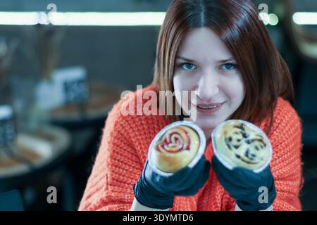Plan frontal d'une personne en tricot orange et gants présentant deux petits pains sucrés artistiques Banque D'Images