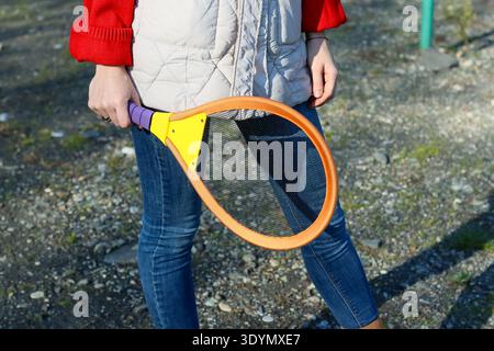 Vue arrière d'une personne en vêtements décontractés tenant la raquette orange vers le bas sur un sol galbé avec des éléments distants Banque D'Images