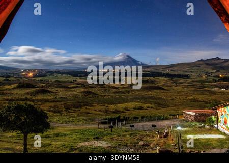 Paysage nocturne longue exposition du volcan Cotopaxi enneigé sous un ciel étoilé en Équateur. Les lumières des villages ruraux illuminent les Andes. Banque D'Images