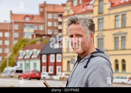 Homme adulte tenant un smartphone tout en se tenant à l'extérieur dans une rue de la ville européenne avec des bâtiments historiques colorés. Concept de communication mobile. Banque D'Images
