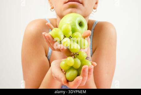 Jeune femme tenant une pomme verte fraîche et des raisins dans ses mains. Nourriture biologique saine, mode de vie végétalien et concept de nutrition sur fond blanc Banque D'Images