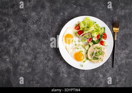 Petit-déjeuner sain avec œufs au plat, salade fraîche et toast au houmous sur fond sombre. Vue de dessus Banque D'Images