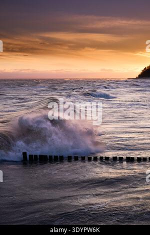 Vue spectaculaire d'une puissante vague océanique s'écrasant contre des groynes en bois par un matin d'hiver orageux au lever du soleil, avec un ciel vibrant et coloré au-dessus de Kos Banque D'Images