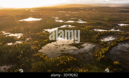 Vue aérienne de la lumière dorée du soleil embrassant les lacs sereins et les forêts boréales, projetant de longues ombres à travers le paysage tranquille, Enontekiö Kilpisjärvi, Banque D'Images