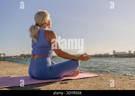 Yoga femme Beach Meditation - Une femme en vêtements bleus pratique le yoga sur un tapis rose à la plage. Banque D'Images