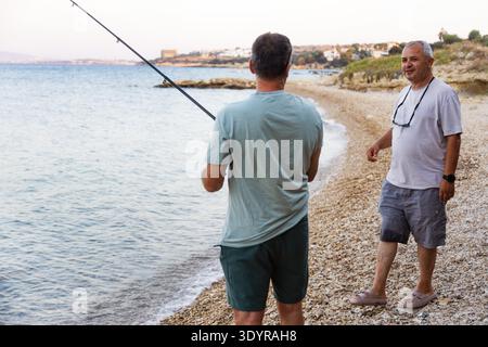 Deux hommes pêchant et parlant sur une plage rocheuse Banque D'Images