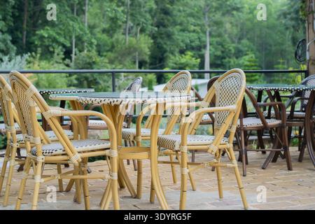 Salle à manger extérieure vide avec chaises en rotin entourées de verdure. Chaises et tables à l'extérieur. Banque D'Images