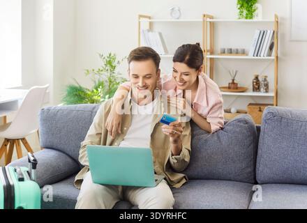 Jeune couple réservant des vols à la maison avec ordinateur portable, carte de crédit et bagages Banque D'Images