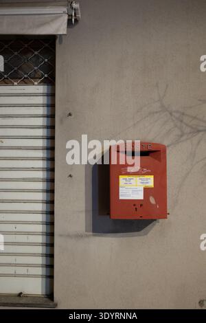 Boîte aux lettres murale rouge sur une façade de bâtiment urbain beige avec volet métallique. Banque D'Images