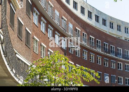 Vue sur le bâtiment en briques rouges avec fenêtres symétriques et balcons en fer noir contraste avec l'arbre vert au premier plan, Oslo, Oslo, Norvège. Banque D'Images