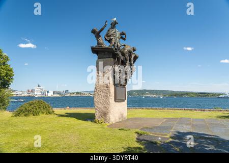 Vue d'une sculpture en bronze sur un piédestal en pierre se dresse en contraste frappant avec la mer et le ciel bleus vibrants, encadrés par l'herbe verte, Oslo, Oslo, Norwa Banque D'Images