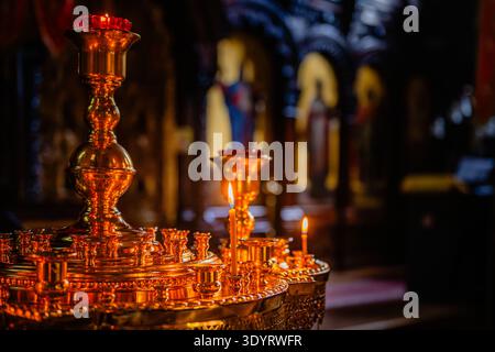 Un candélabre orthodoxe doré avec des bougies de prière allumées dans un intérieur sombre de l'église, avec un bokeh chaud et des détails en laiton complexes. Banque D'Images