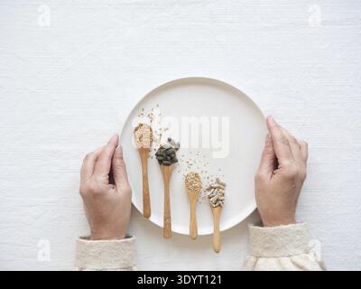 Femme tenant une assiette avec des graines de lin, de citrouille, de sésame et de tournesol dans des cuillères pour le cycle des graines Banque D'Images