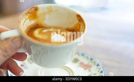 Tasse à café cappuccino presque finie avec latte art tenu à la main sur une table en bois Banque D'Images