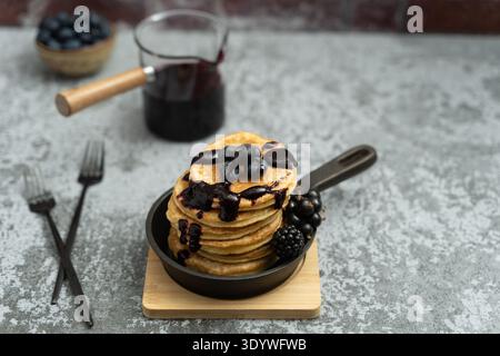 Pile de crêpes avec filet de confiture et myrtilles sur la poêle avec pot de confiture dans la scène de petit déjeuner rustique. Banque D'Images