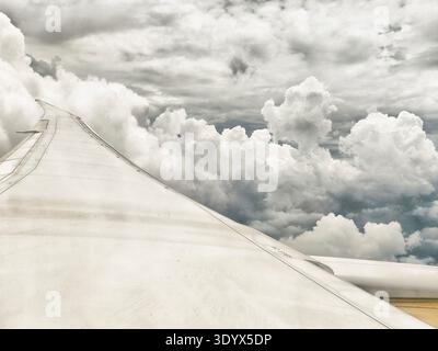 Vue depuis la fenêtre de l'avion montrant les ailes et les nuages dans le ciel avec la lumière du soleil créant contraste et texture dans les formations nuageuses moelleuses. Banque D'Images