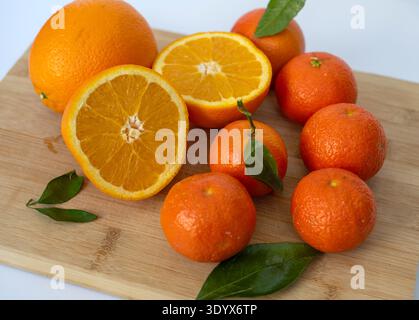Agrumes frais comprenant des oranges et des mandarines avec des feuilles vertes disposées sur une planche à découper en bois. Nourriture naturelle saine riche en vitamine C. Banque D'Images