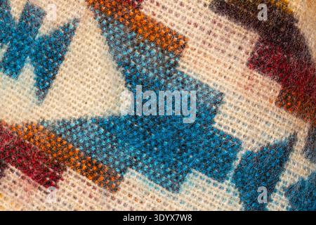 Macro gros plan de tissu textile tissé à la main traditionnel montrant un motif géométrique coloré en bleu, orange et beige avec des fibres de laine détaillées. Banque D'Images