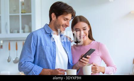 Couple apprécie le café du matin tout en regardant smartphone dans Cozy Kitchen Banque D'Images
