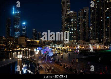 Une vue nocturne d'une promenade moderne en bord de mer urbaine bordée de gratte-ciels illuminés. La passerelle pavée courbe le long de l'eau, avec décora Banque D'Images