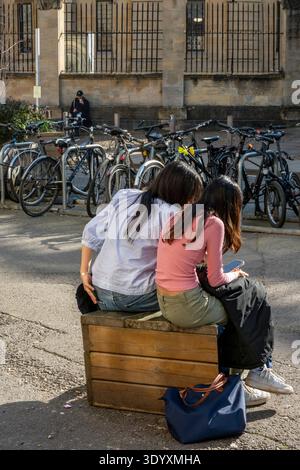 Deux jeunes étudiantes de l'Université d'Oxford assis sur un banc dans le centre-ville d'Oxford à côté d'une rangée de vélos par un jour ensoleillé de printemps Banque D'Images