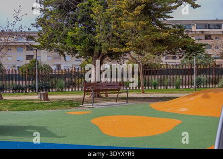 Parc urbain avec un banc en bois et un sol résilient avec des bâtiments en arrière-plan Banque D'Images