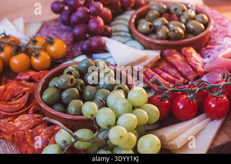 Plateau de charcuterie avec olives, raisins, charcuteries et fromages disposés sur une table rustique en bois pour les tapas de style méditerranéen Banque D'Images