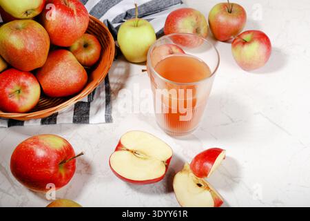 Vue de dessus d'un verre de jus de pomme frais sur une surface en marbre, entouré de pommes rouges entières et tranchées dans un panier en osier avec une serviette rayée. Élevé Banque D'Images
