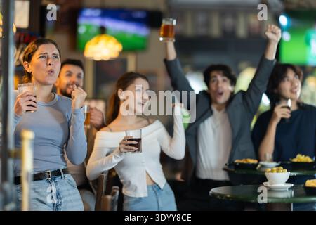 Groupe d'amis célébrant la victoire de l'équipe tout en regardant un match sportif Banque D'Images