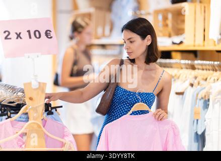 La cliente fille choisit chemisier dans le magasin, et l'acheteur examine soigneusement le produit. Banque D'Images