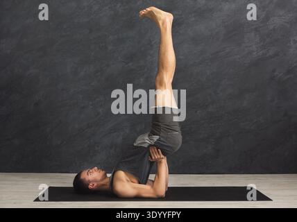 Jeune homme en classe de yoga faisant une épaule debout Banque D'Images