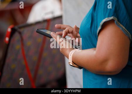 Femme utilisant un smartphone sur le marché, absorbé dans l'écran mobile, utilisateur de smartphone concentré, texture de peau de main, gros plan. Banque D'Images