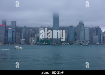 Un traversier traverse le port Victoria en face de la ligne d'horizon de l'île de Hong Kong entourée de brouillard, vue depuis Tsim Sha Tsui, Kowloon, Hong Kong. Banque D'Images