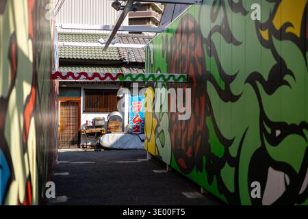 Une ruelle étroite encadrée de peintures murales colorées menant à un bâtiment traditionnel à Nakazakicho, Osaka, Japon. Banque D'Images