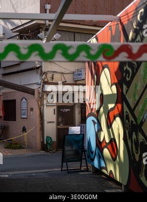 Un petit bâtiment sur une ruelle tranquille encadrée par des panneaux peints décoratifs à Nakazakicho, Osaka, Japon. Banque D'Images