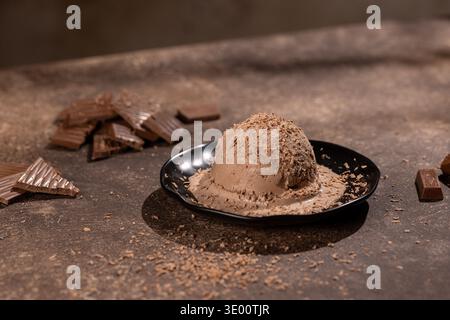 Gros plan d'une grande boule de crème glacée au chocolat crémeuse, saupoudrée de copeaux de chocolat fins, sur une assiette noire mate. Le studio stylé tourné à la guerre Banque D'Images