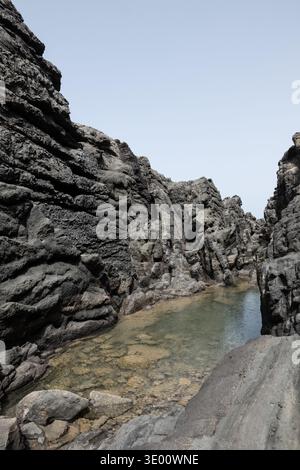 Piscine naturelle claire formée entre les roches volcaniques sombres de lave le long de la côte d'Aguas Verdes à Fuerteventura Canaries côte atlantique escarpée et Banque D'Images