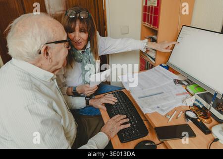 Femme aidant son père aîné à naviguer dans la technologie informatique et les tâches en ligne Banque D'Images