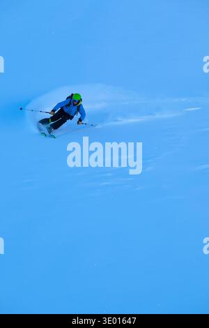 Un skieur sculpte dans la poudre fraîche avec des équipements vibrants, pulvérisant de la neige sous un ciel bleu vif. Le mouvement rapide et contrôlé transmet l'énergie, l'habileté et le frisson du sport d'hiver dans les montagnes. || autorisation du modèle Banque D'Images