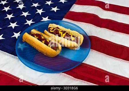 Une présentation patriotique de deux délicieux hot-dogs, généreusement recouverts de ketchup et de moutarde, reposant sur une plaque bleue éclatante avec le drapeau américain comme un Banque D'Images