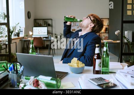 Jeune homme caucasien buvant de la bière au bureau pendant Workday Banque D'Images