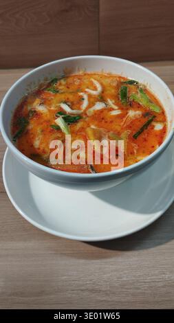 Authentique soupe thaïlandaise tom yum servie dans un bol blanc sur une table en bois. La célèbre soupe de fruits de mer chaude et aigre représente la culture traditionnelle de la cuisine thaïlandaise Banque D'Images